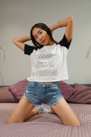 Lina Lee in a T-shirt and a pair of short jeans plays on her bed and gets naughty